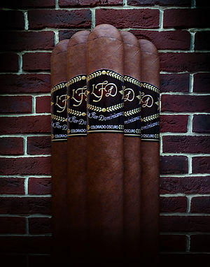 Four La Flor Dominicana Colorado Oscuro cigars with black-and-gold LFD bands against a brick wall
