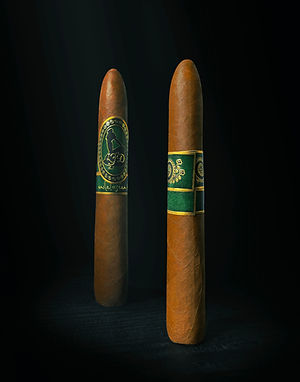 Two La Flor Dominicana Andalusian Bull cigars standing on a dark background, each with green bands