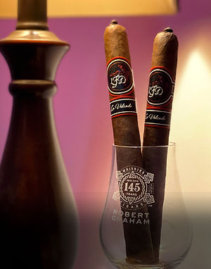 Two La Flor Dominicana cigars with LFD bands placed upright in a glass next to a lamp.