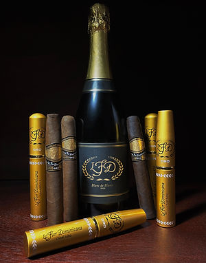 La Flor Dominicana Oro cigars with gold tubes and a bottle on a dark surface