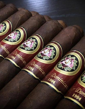 Close-up of five La Flor Dominicana cigars with red and gold bands labeled 1994 lying on a dark surface.