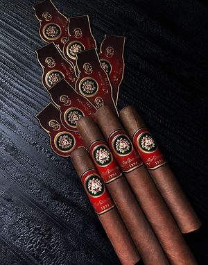 Four La Flor Dominicana cigars with red floral bands displayed next to several detached bands on a black background.